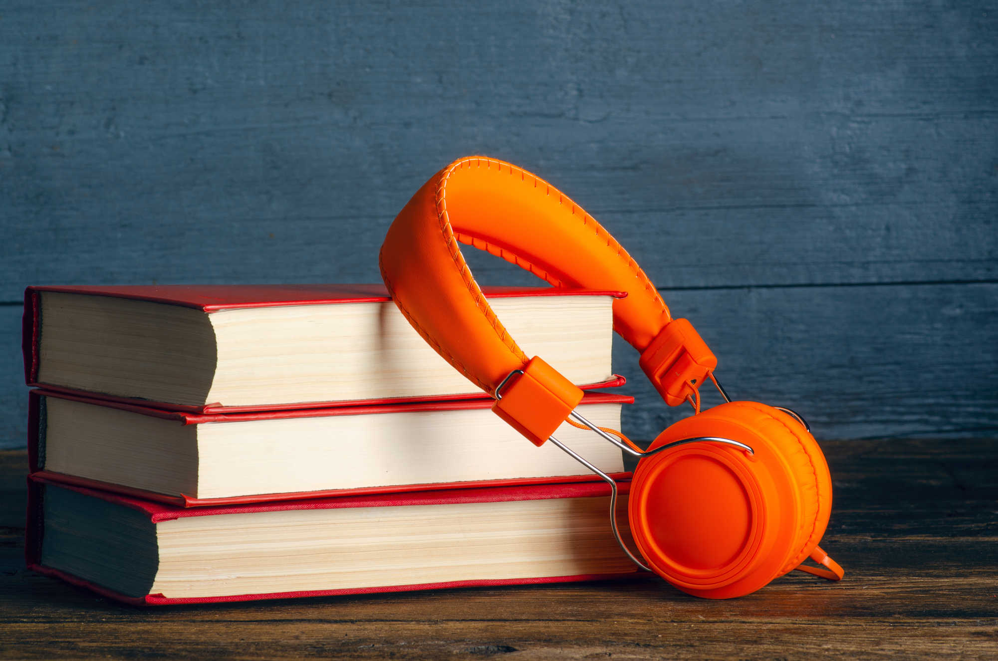 Modern headphones with stack of books on wooden background table. Space for text